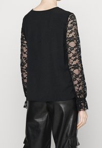 Haut noir avec manches longues en dentelle ornées de motifs floraux ; corps lisse avec une coupe décontractée, associé à un pantalon en similicuir noir.