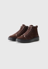 Brune semskede høye sneakers med svarte gummisåler, med snøringer foran, glidelås på siden, og logo på tungen og hælen.