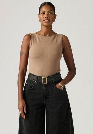 Beżowy top bez rękawów w połączeniu z szerokimi czarnymi spodniami dżinsowymi i czarnym paskiem ze złotą klamrą. Minimalistyczny design, gładka faktura.