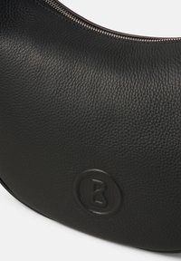 Borsa a tracolla in pelle nera con finitura texture, forma a mezzaluna e logo circolare impresso. Presenta una cerniera argentata lungo la parte superiore.