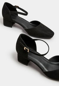 Svarta mocka låga klackskor med spetsig tå och ankelsnärning, med en accent i guldspänne. Slät yta och minimalisk design.