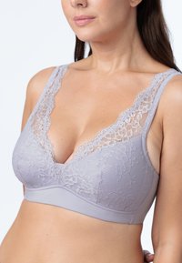 Siva čipkasta bralette s globokim V-izrezom. Mehka tkanina z zapletenimi cvetličnimi detajli na skodelicah in čipkastim obrobom ob naramnicah.