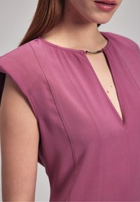 Robe violette avec un décolleté en V, des épaules structurées et une touche dorée au niveau du cou. Le tissu a une texture lisse avec un léger éclat.