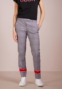 Pantaloni a quadri neri, bianchi e rossi con vestibilità slim, caratterizzati da un dettaglio rosso all'orlo. Abbinati a una camicia nera a maniche corte.
