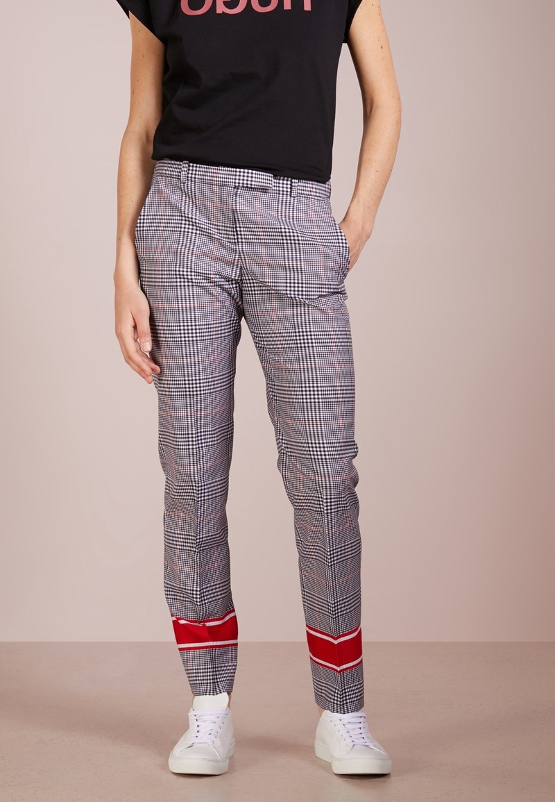 Pantaloni a quadri neri, bianchi e rossi con vestibilità slim, caratterizzati da un dettaglio rosso all'orlo. Abbinati a una camicia nera a maniche corte.