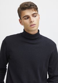 Mørkeblå turtleneck genser laget av mykt strikkemateriale, med en fitted design som har ribbestrikket krage og lange ermer.