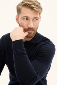 Navyblaues Strickpolo aus leichtem Stoff mit einem Kragen. Die Hand des Models ruht auf dem Kinn und zeigt den Ärmel und die Textur.