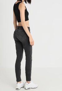 Top corto negro con textura acanalada, combinado con jeans ajustados de color gris oscuro. La modelo lleva zapatillas deportivas blancas y el cabello estilizado en un corte corto.