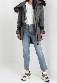 Grå rutmönstrad parkas med svarta detaljer och huva av konstgjord päls, kombinerad med ljusblå raka jeans och färgglada klumpiga sneakers.