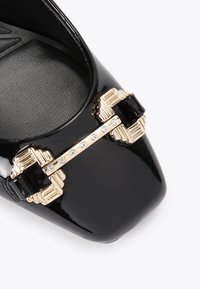 Czarne lakierowane buty z kwadratowym noskiem, z akcentem w postaci złotej klamry zdobionej przezroczystymi kryształkami. Teksturowana wkładka dla lepszej przyczepności.