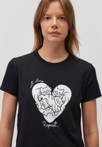 Schwarzes Baumwoll-T-Shirt mit einem weißen Grafikdesign von vier Katzen in einem Herz, mit dem Text "Essen. Schlafen. Wiederholen." in einer verspielten Schriftart.