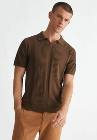 Polo shirt marrone a maniche corte con righe verticali texture, colletto a V e orlo a coste. Abbinato a pantaloni beige.