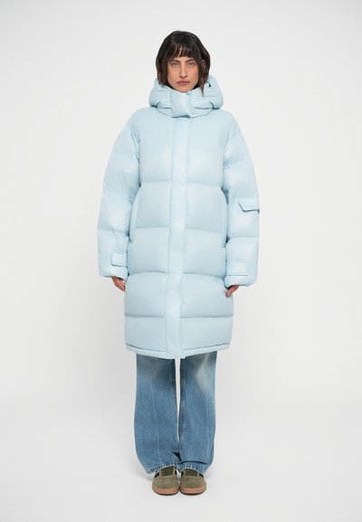 Chaqueta acolchada azul claro con un cuello alto, forma oversize y textura acolchada; combinada con jeans de mezclilla acampanados y zapatillas verdes.