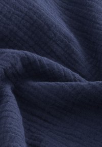 Tkanina tamnoplave boje sa teksturiranim, mrežastim uzorkom i mekim završetkom, prikazuje nabore i nabiranja materijala.