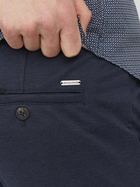 Tamno plave hlače od teksturirane tkanine, s kopčanjem na gumb i srebrnom oznakom "JACK & JONES" na džepu.