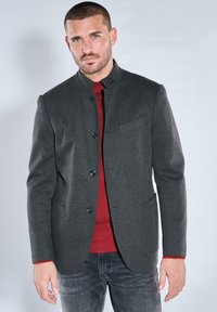 Gray blazer with a mandarin collar, black buttons, and a chest pocket, layered over a red ribbed sweater. Worn with dark jeans.