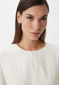 Lightweight white blouse with a rounded neckline and a narrow front zipper, featuring long sleeves and a smooth texture.