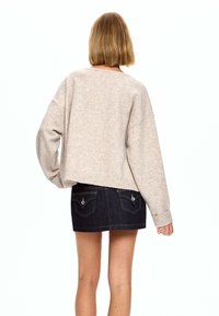 Béžov pulover s prekomerno velikostjo, pleten z padlimi rameni, rebrastimi manšetami in robom. V kombinaciji s temno denim mini krilom z detajli žepov.