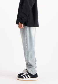 Lichtblauwe spijkerbroek met een relaxte pasvorm, gecombineerd met een zwart shirt met lange mouwen en zwarte sneakers met witte strepen en accenten.