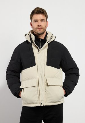 Puffer jacket featuring a black upper section and cream lower section. Equipped with a hood, two front pockets, and zipper closure. Soft texture.