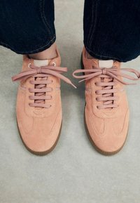 Roze zamšaste tenisice s odgovarajućim vezicama, s okruglim vrhom i gumeni potplat. Ukrašene su suptilnim detaljima šivanja.