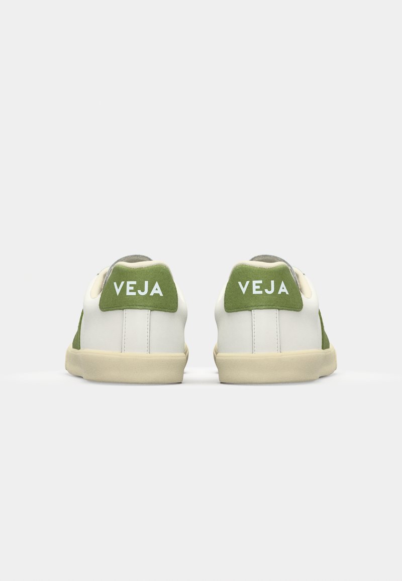 Baskets blanches avec des accents en suede vert. Présente un marquage "VEJA" en relief sur le talon et une semelle texturée couleur crème.