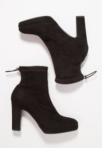 Bottes à cheville en daim noir avec un talon bloc haut, une fermeture éclair latérale, une tige ajustée et une texture lisse ; design minimaliste sans motifs visibles.