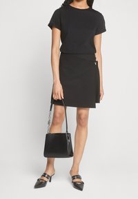 Atasan hitam lengan pendek, rok lilit pinggang tinggi, sepatu mules hitam dengan aksen, dan tas tangan hitam dengan tali rantai. Semua potongan berwarna monokrom.