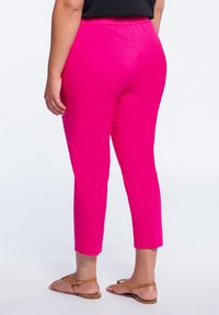 Fuchsianfärgade byxor i stretchbomull med elastisk midja, beskuren längd och uppvikta fållar, sedd från baksidan.