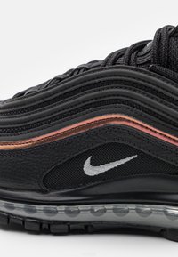 Black athletic shoe with textured leather and mesh, featuring a wavy design, orange accent, and visible air cushioning in the sole.