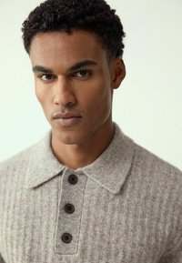 Graues, geripptes Polohemd aus Strick mit Kragen und drei dunklen Knöpfen, geprägt von einer weichen Textur und subtilen Farbnuancen.