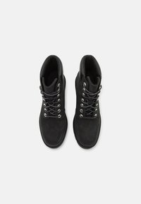 Black suede ankle boots with a textured finish, featuring metal eyelets and black laces, designed for robust support and comfort.