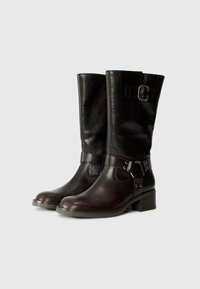 Braune Lederstiefel bis zum Knie haben eine abgerundete Zehe, einen Riemen mit einer dekorativen Schnalle und einen niedrigen, gestapelten Absatz für Stabilität.