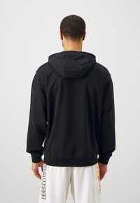 Felpa nera con cappuccio e coulisse, maniche lunghe e polsini a coste. Tessuto morbido con design minimalista, senza loghi visibili.
