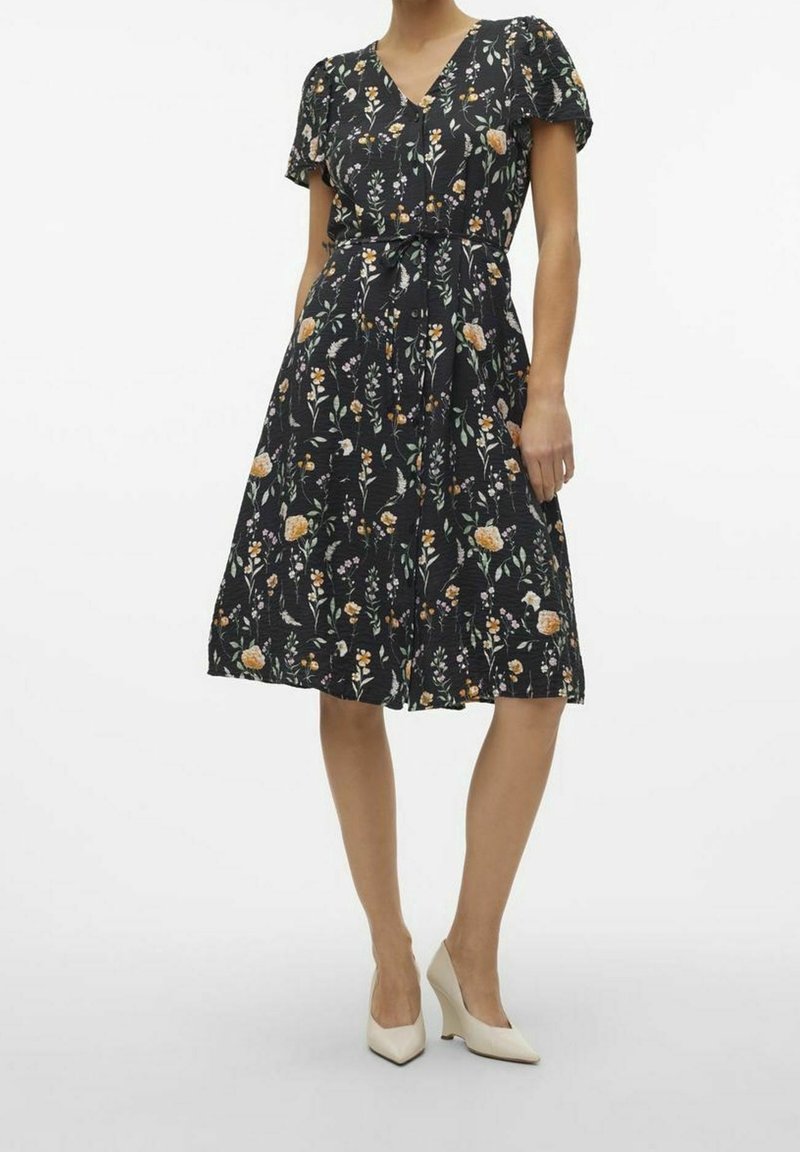 Robe fleurie avec un fond noir, manches courtes bouffantes, col en V, ceinture à la taille, jupe évasée et poches latérales. Ornée de fleurs de différentes couleurs.