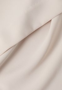 Tissu texturé beige avec une surface lisse et douce, présentant un léger éclat et un motif côtelé uniforme. Drapé en plis.