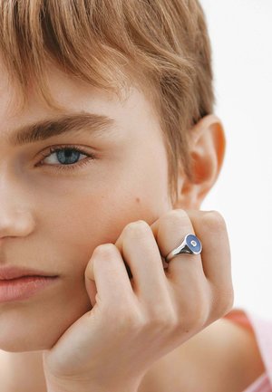 Anillo de plata con un acento redondo azul en el centro, con una superficie suave y pulida y un diseño contemporáneo.