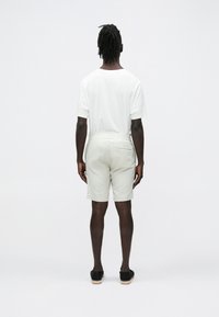 Wit t-shirt met korte mouwen en lichtgrijze korte broek met elastische tailleband, voorzien van een achterzak, gedragen met zwarte espadrilles.