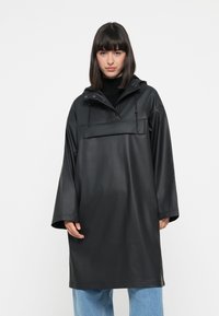 Black waterproof coat with a hood, front pocket, and drawstring. Features wide sleeves and a loose fit, made from smooth, matte material.