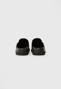 Crne cipele na slip-on s glatkom, sjajnom površinom, zaobljenim dizajnom i ravnim potplatom. Nema vidljivog hardvera ili uzoraka.