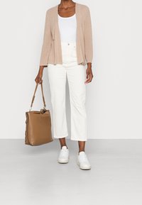 Beige cardigan med öppen front, vit tanktopp, höga vita jeans och en brun läderhandväska. Vita sneakers fulländar outfiten.