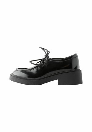 Scarpe in pelle verniciata nera con punta arrotondata, suola in gomma piatta e design con lacci. Presentano una superficie texture e uno stile minimalista.