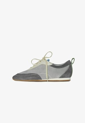 Šedé semišové tenisky s bílým koženým akcentem, kulatou špičkou, šněrováním a zeleným poutkem na patě. Vyznačují se kontrastními texturami a detaily prošívání.