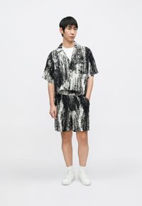 Kurzärmliges schwarz-weiß gemustertes Hemd und Shorts Set aus leichtem Stoff, mit lockerem Schnitt und feiner Textur. Weiße Sneakers.