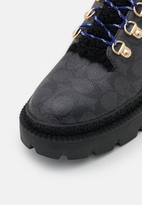 Stivale nero con texture, dotato di una tomaia decorata, con occhielli in metallo dorato e lacci blu. Suola in gomma nera spessa con battistrada robusto.