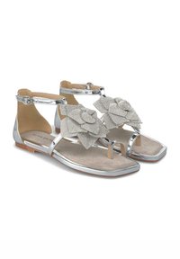 Sandali metallici argento con decorazioni floreali, suole piatte e cinturini alla caviglia. Presentano una superficie liscia e lucida e una soletta imbottita.