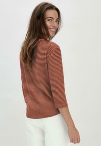 Rustfarbene langärmelige Bluse mit weißen Streifen, leichtes Gewebe, runder Ausschnitt und Dreiviertelärmel. Glatte Textur, lässige Passform.