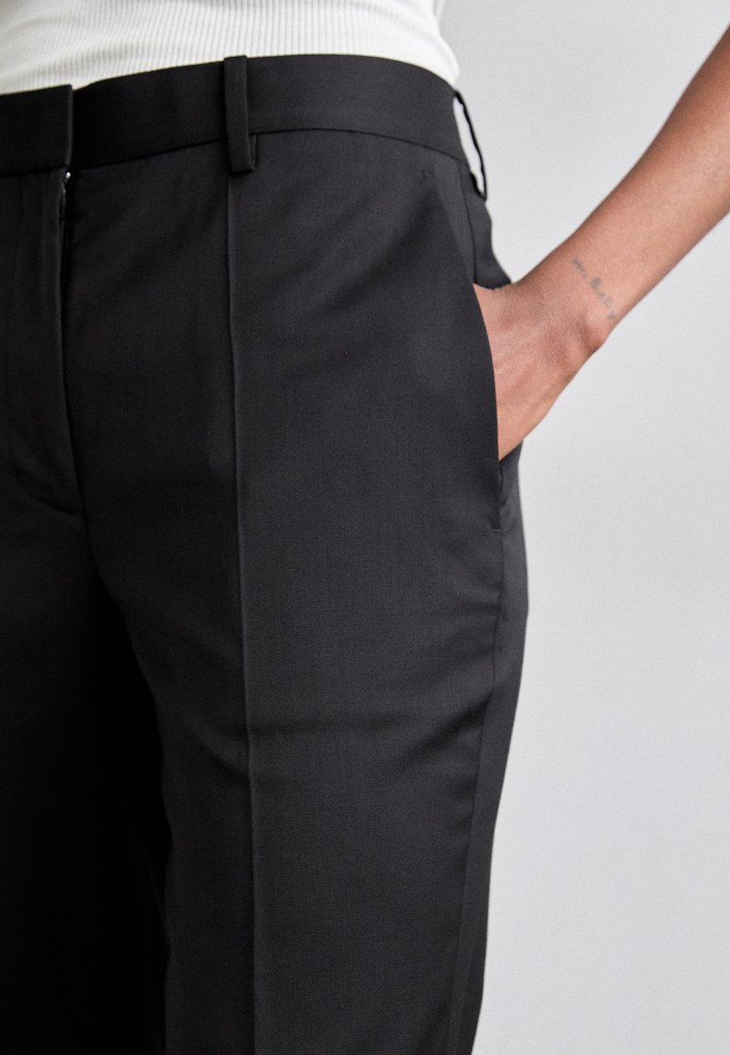 Black tailored trousers with a sleek, smooth texture and side pockets. The waistband is flat and slightly elevated.