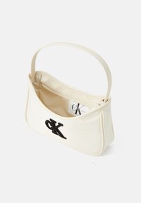 Sac �à main en cuir blanc avec un design incurvé, featuring un logo brodé noir, une fermeture éclair supérieure et une seule poignée.