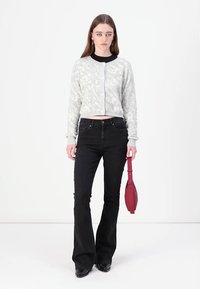 Grå teksturert cardigan med rund hals, knappelukking, sammen med svarte utsvingte jeans og holder en rød veske.
